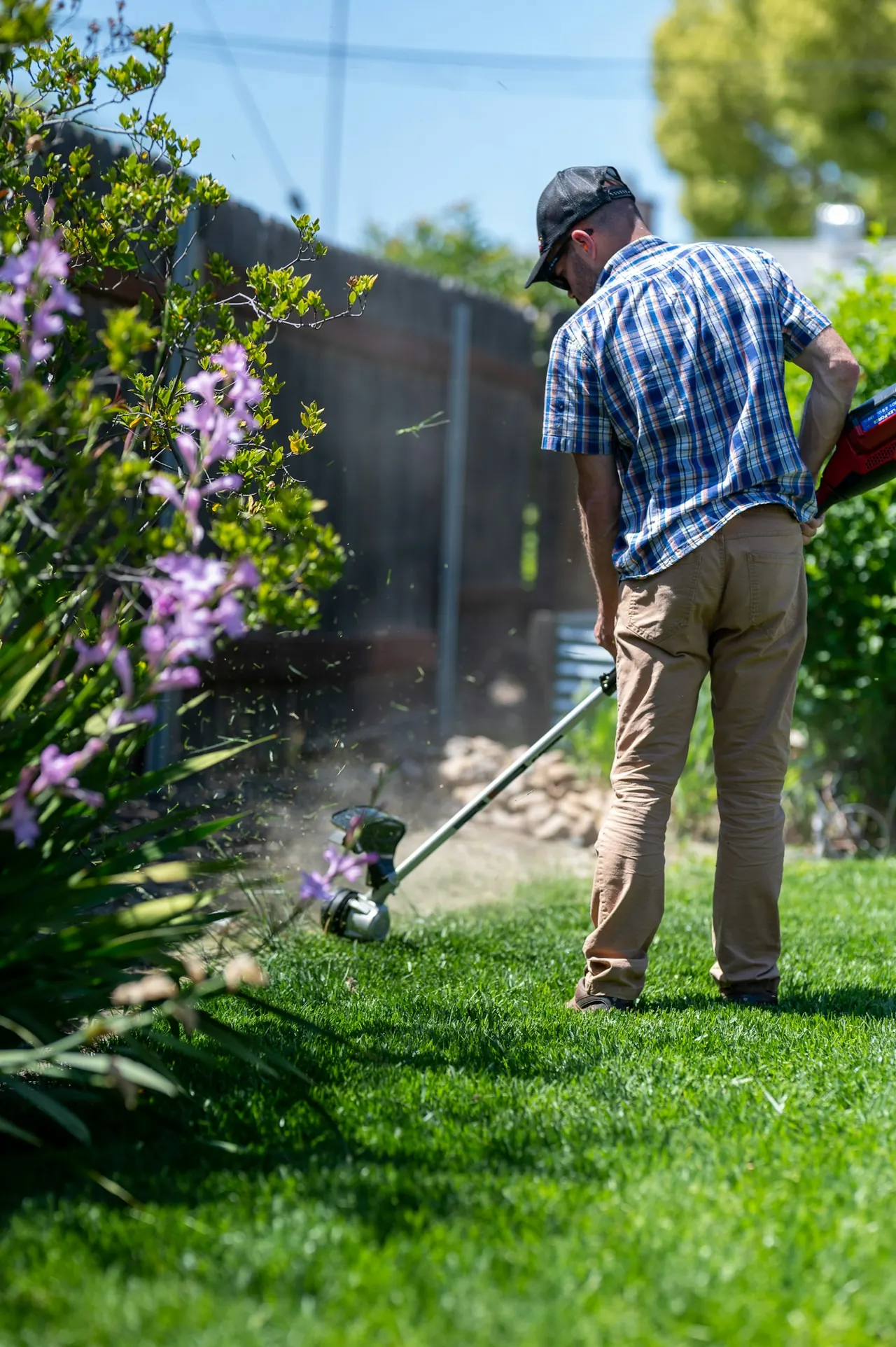 Profissional aparando o gramado de um jardim.