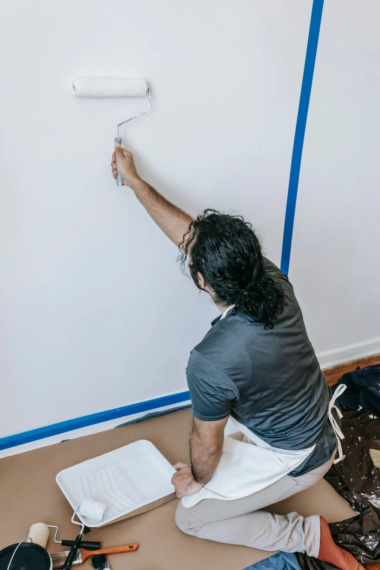 Profissional aplicando tinta em uma parede com rolo e proteção no ambiente.
